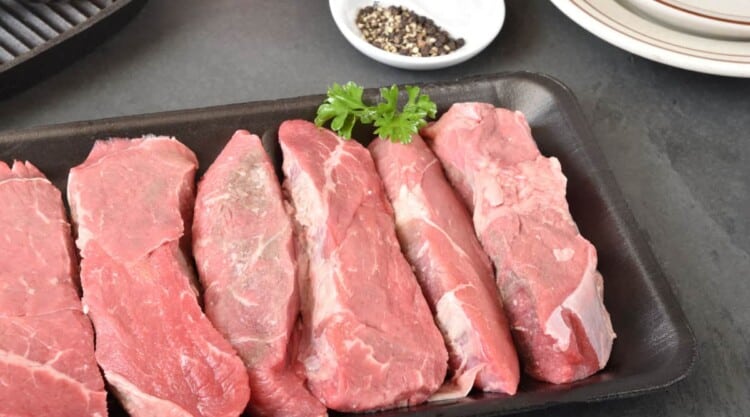 Raw petite sirloin steaks in a tray with one sprig of parsley