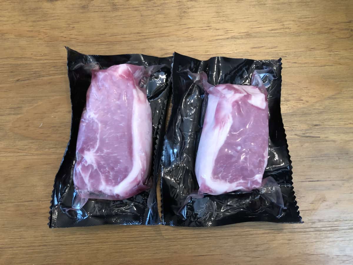 Two porter road pork chops in their packaging, on a wooden table.