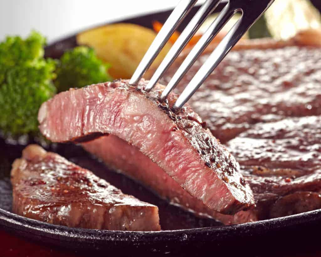 A slice of top sirloin steak held on the prongs of a fork