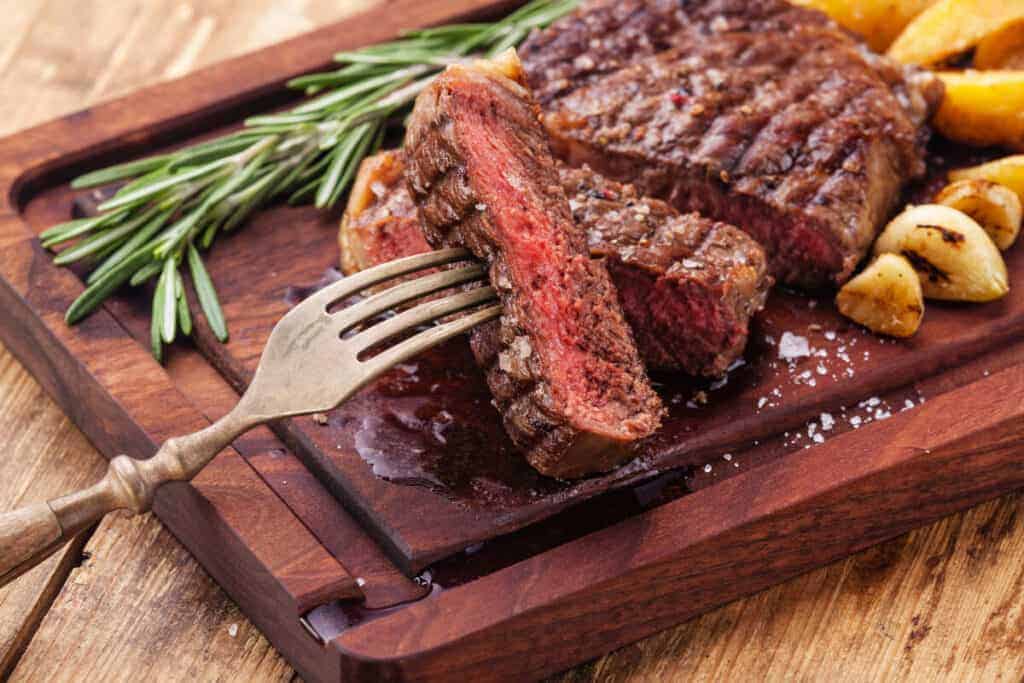 sliced medium rare ribeye steak, with a piece held on a fork