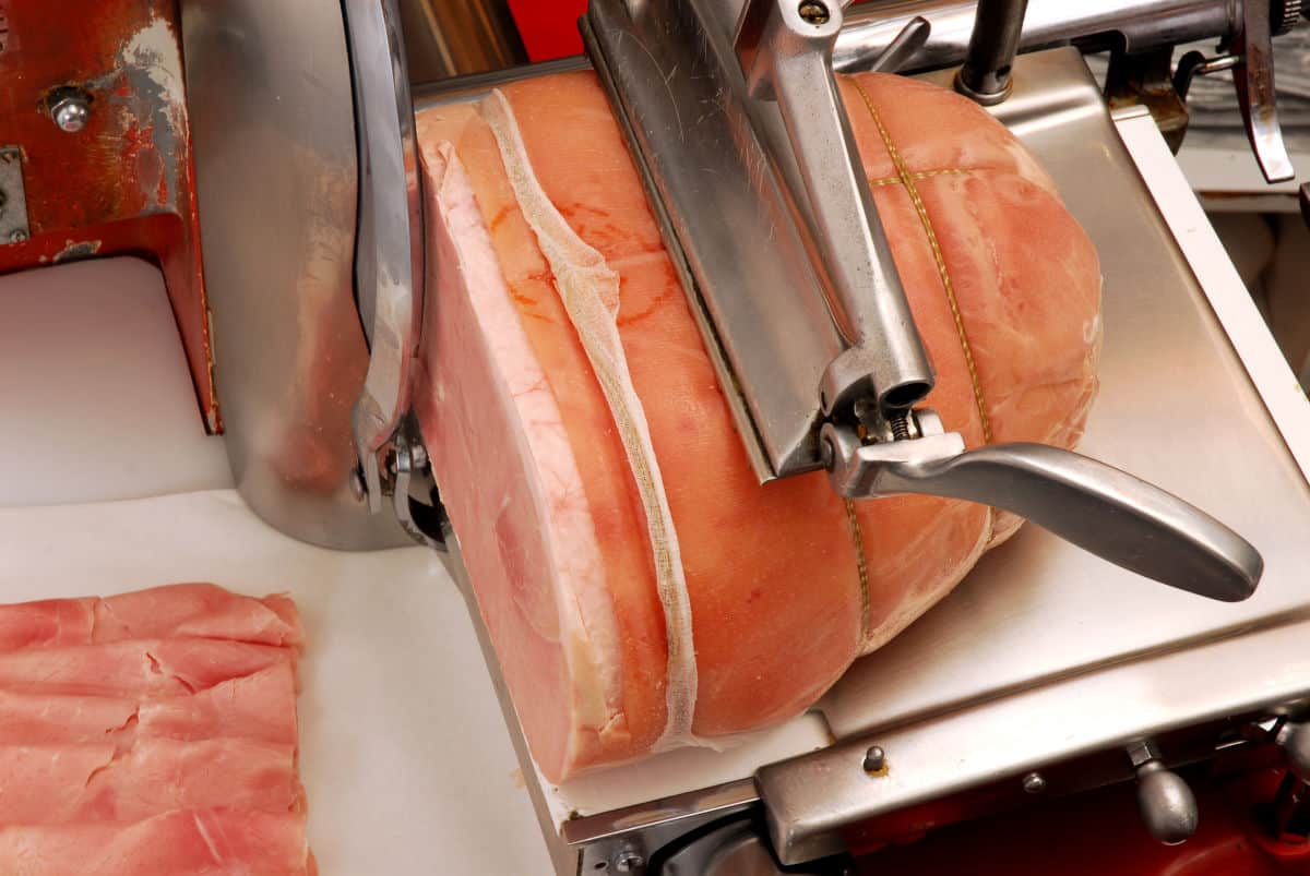 A large piece of ham being put through a food sli.