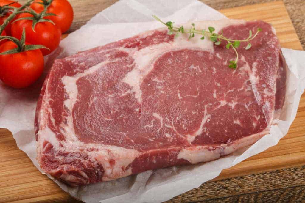 Raw ribeye steak on paper, next to some tomatoes