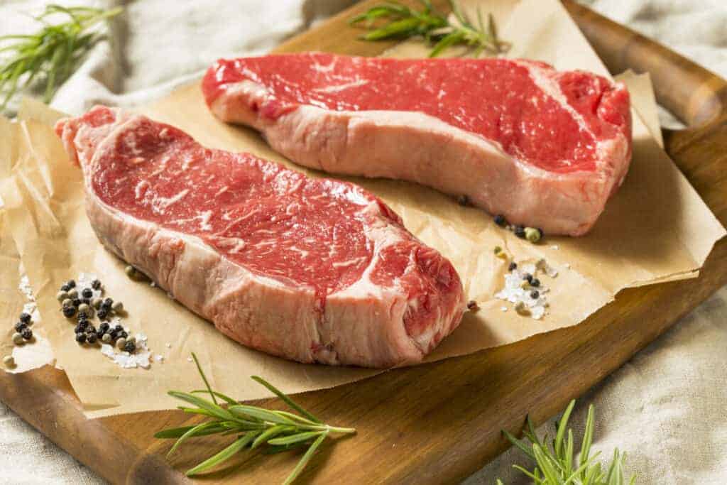 Two raw sirloin steaks on butcher paper surrounded by rosemary spr.