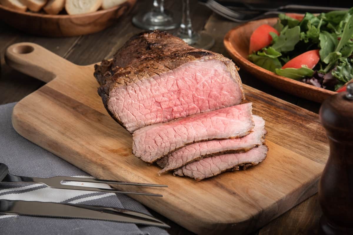 Partially sliced bottom round roast with carving knife and fork .