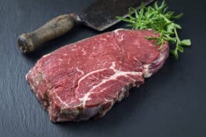 Raw bottom round steak, on a slate cutting board with rosemary and a butchers knife