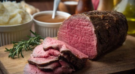 pink, roasted eye of round roast, sliced and sitting on a cutting board.