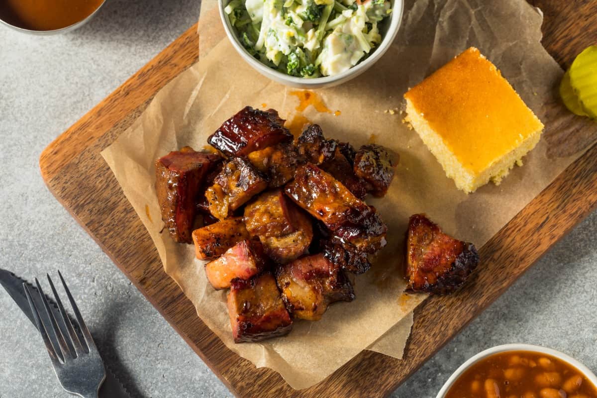 Brisket burnt ends on a cutting board, with corn bread and pit bea.