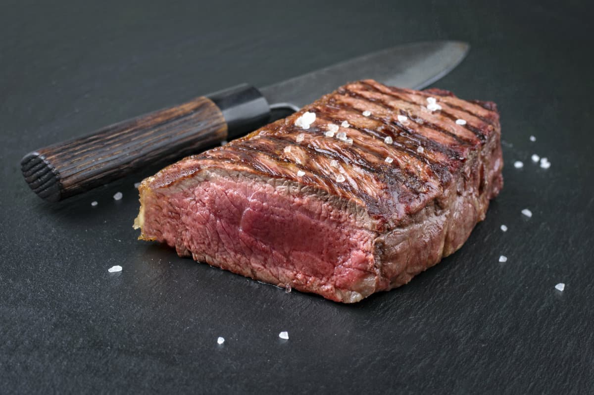 grilled bottom round steak with end sliced off, sitting on a slate surf.