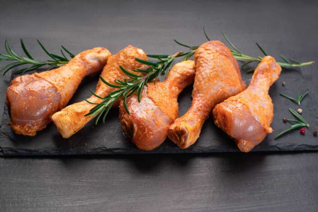 Marinated chicken legs on slate board with some herbs layed on .