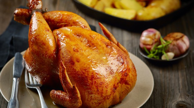 A whole roasted chicken with crispy skin, on a wooden table.
