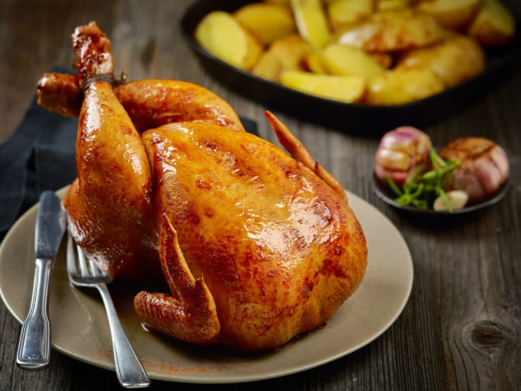 A whole roasted chicken with crispy skin, on a wooden table.