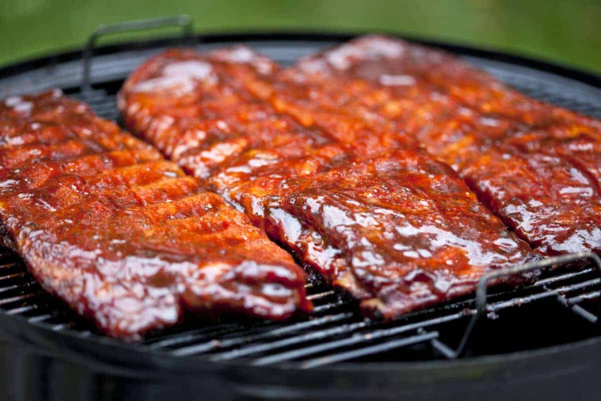 Sauced St Louis ribs sitting on a charcoal grill.