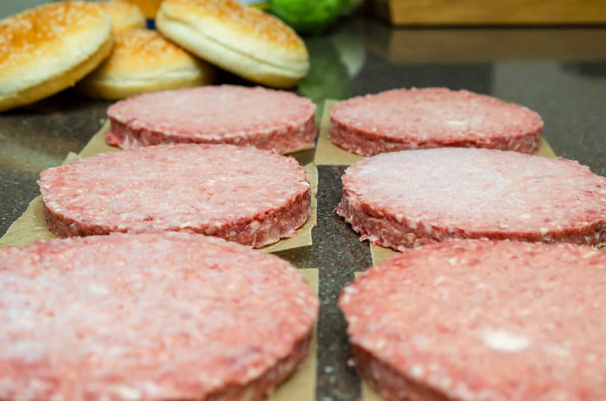 defrosting six frozen burgers sat on parchment paper squares, on the kitchen coun.