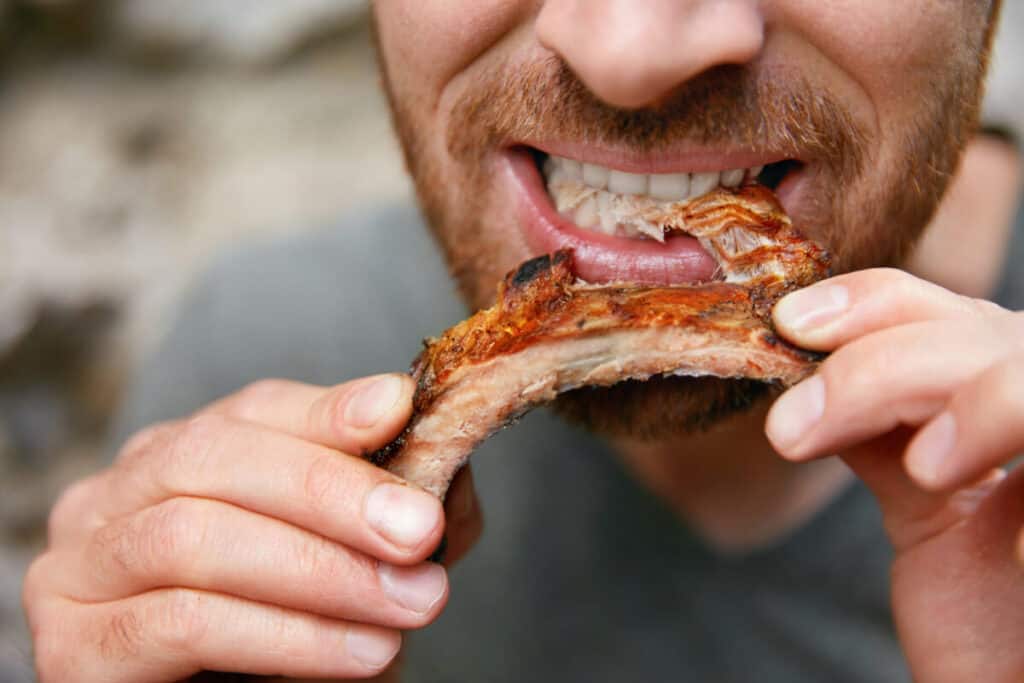 A mans face from the nose down, eating rib meat off the b.