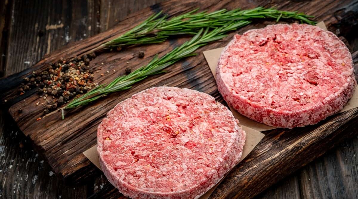 frozen burgers on cutting board with a rosemary sprig in the background.