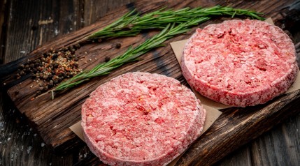 frozen burgers on cutting board with a rosemary sprig in the background.