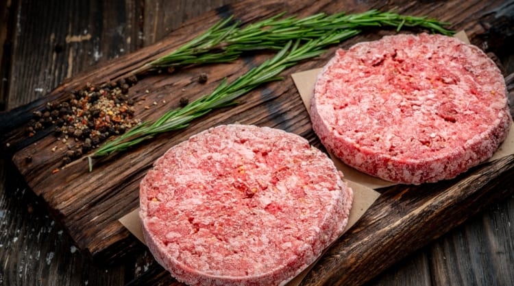 frozen burgers on cutting board with a rosemary sprig in the background.