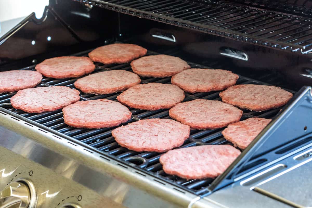 15 frozen burgers laid out on a gas grill
