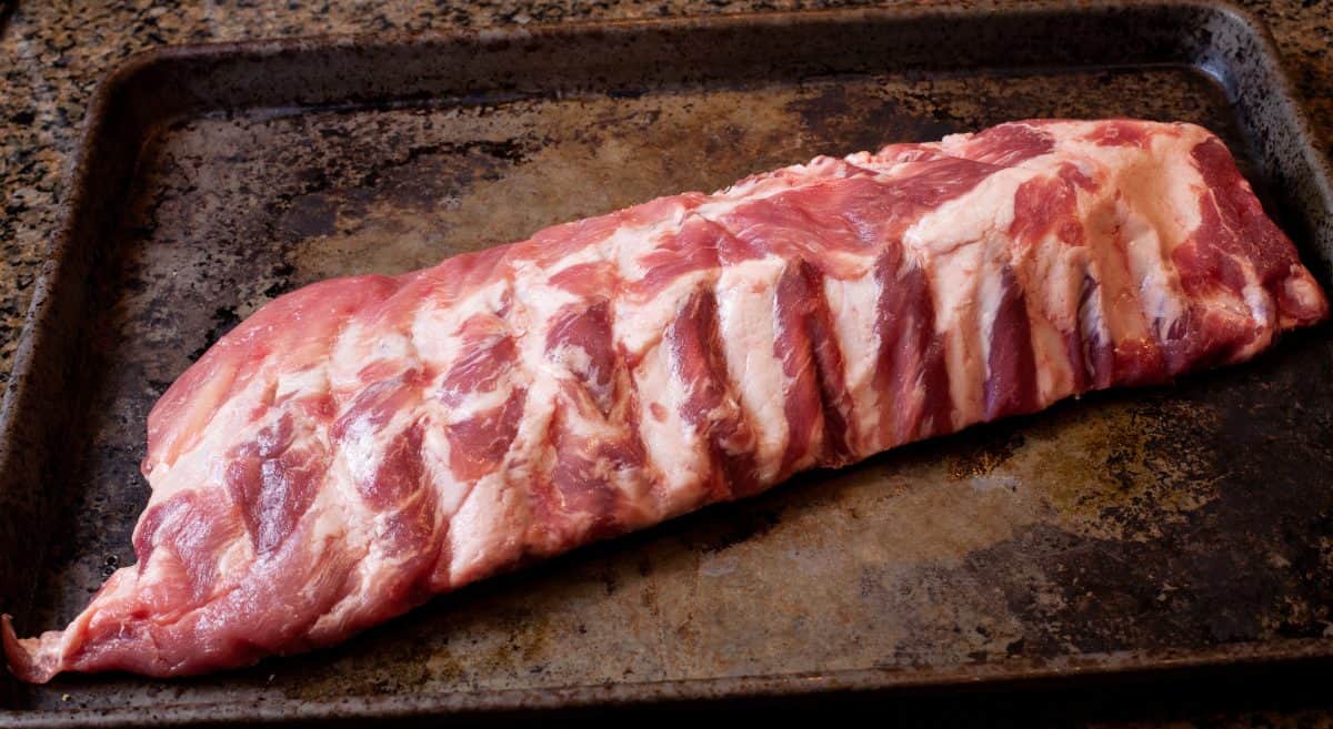 raw baby back ribs, prepped and sitting on a baking tray