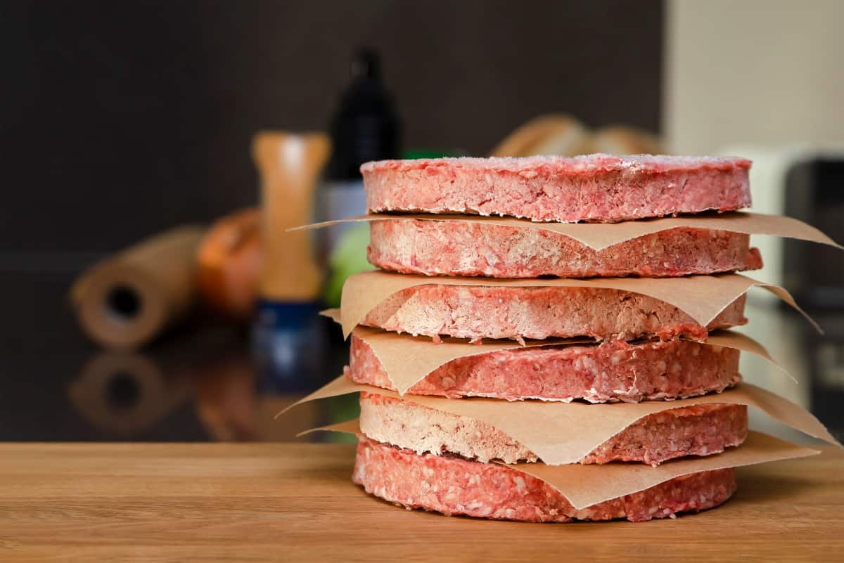 A stack of frozen burgers separated by parchment squa.