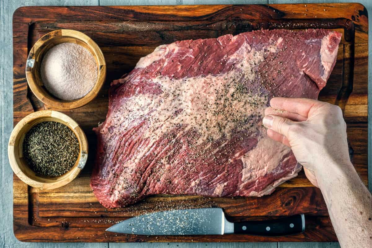 Raw brisket being seasoned with salt and pep.