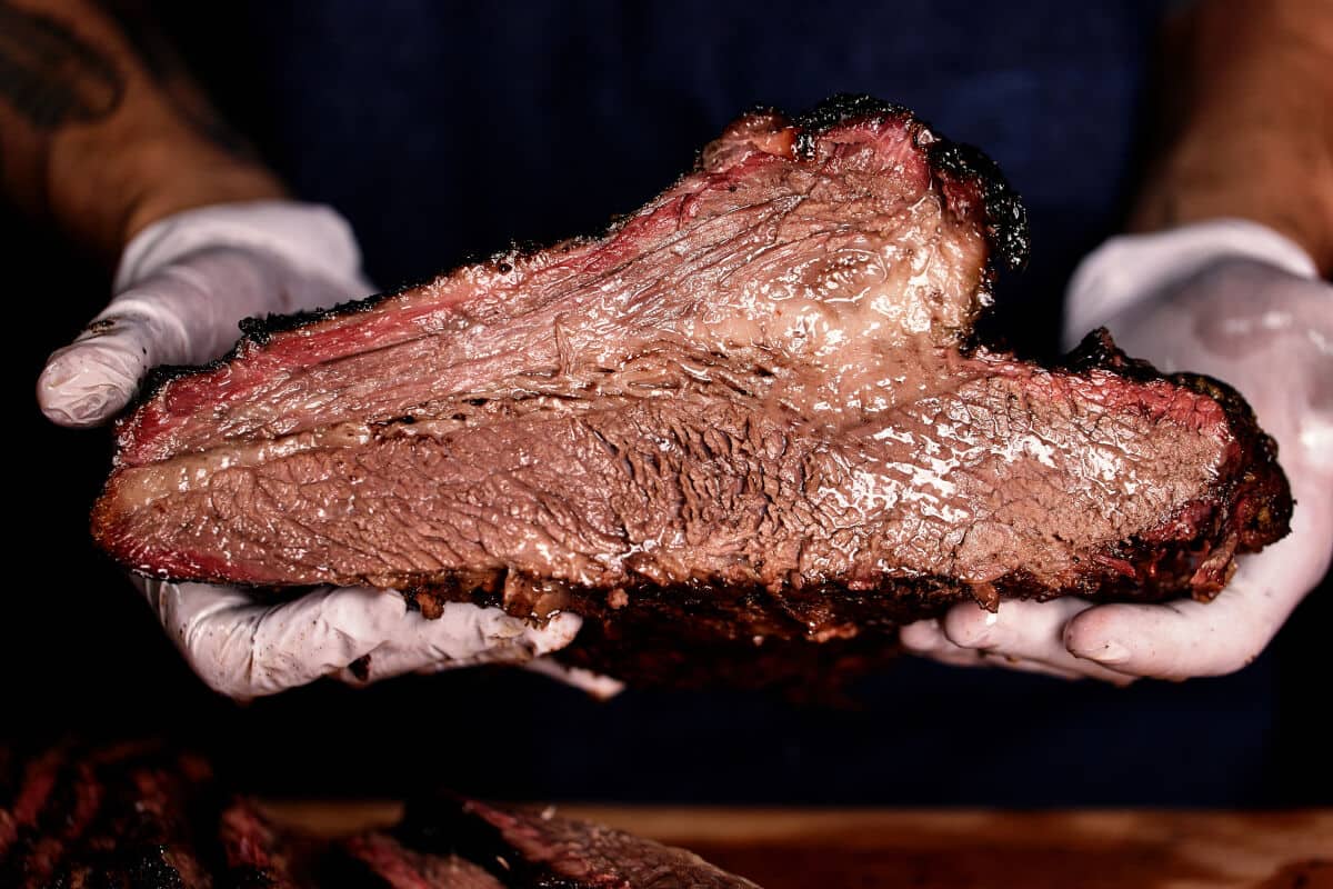 Looking at the sliced end of a halved, smoked brisket being held with white nitrile glov.