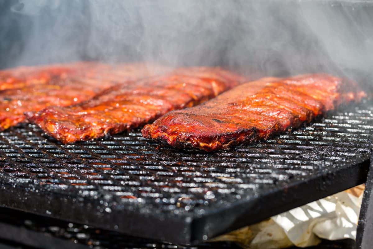 Multiple racks of baby back ribs in a smo.