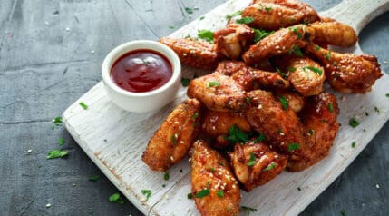 Chicken wings with dip, served on a white, wooden paddle board.