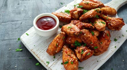 Chicken wings with dip, served on a white, wooden paddle board.