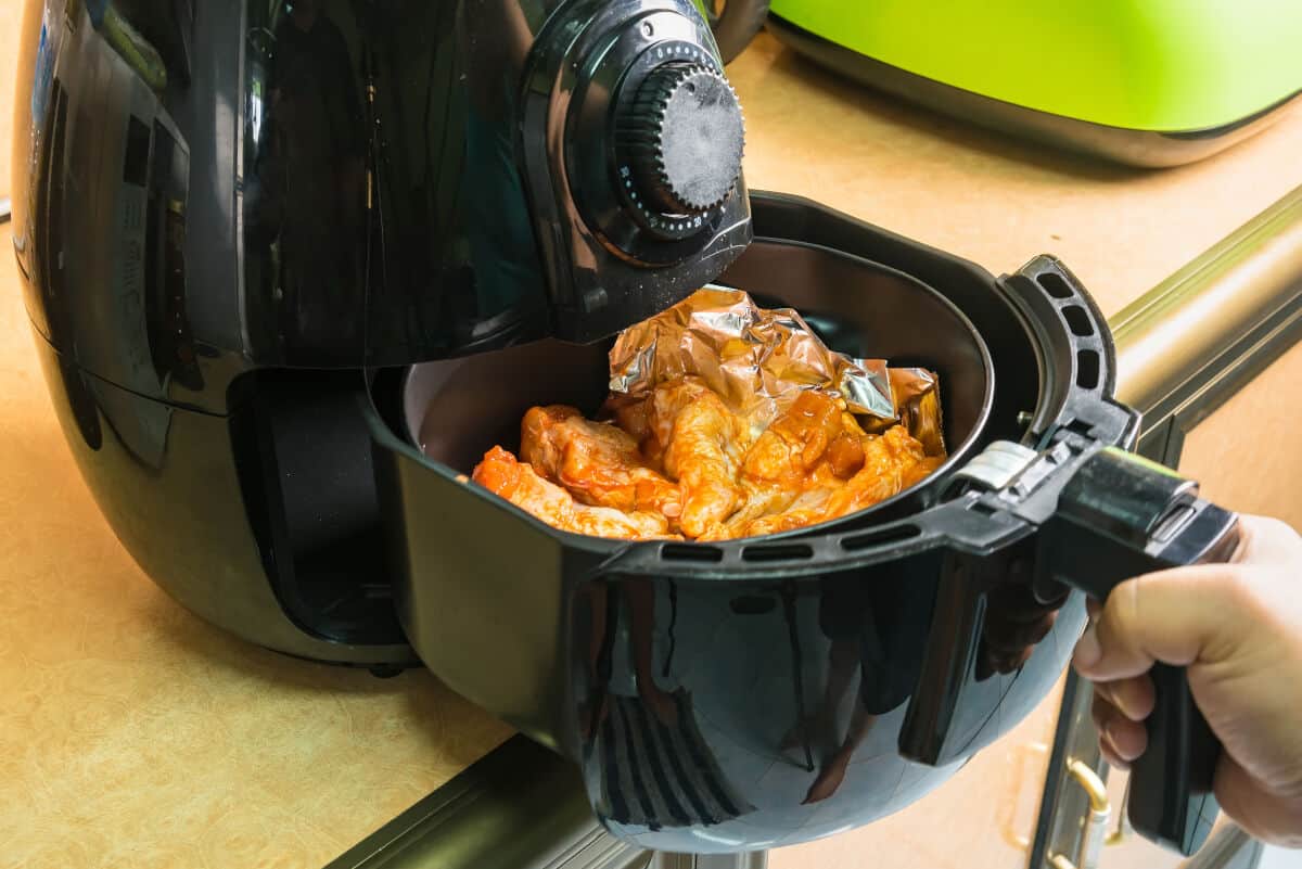 Chicken wings being placed into an a black air fryer on a wooden surf.