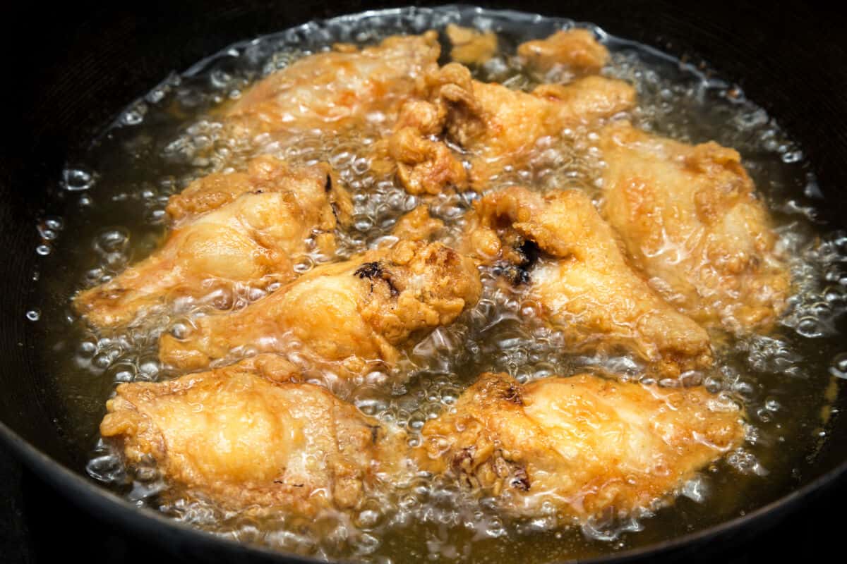 close up of chicken wings in a deep fryer, with oil bubbl.