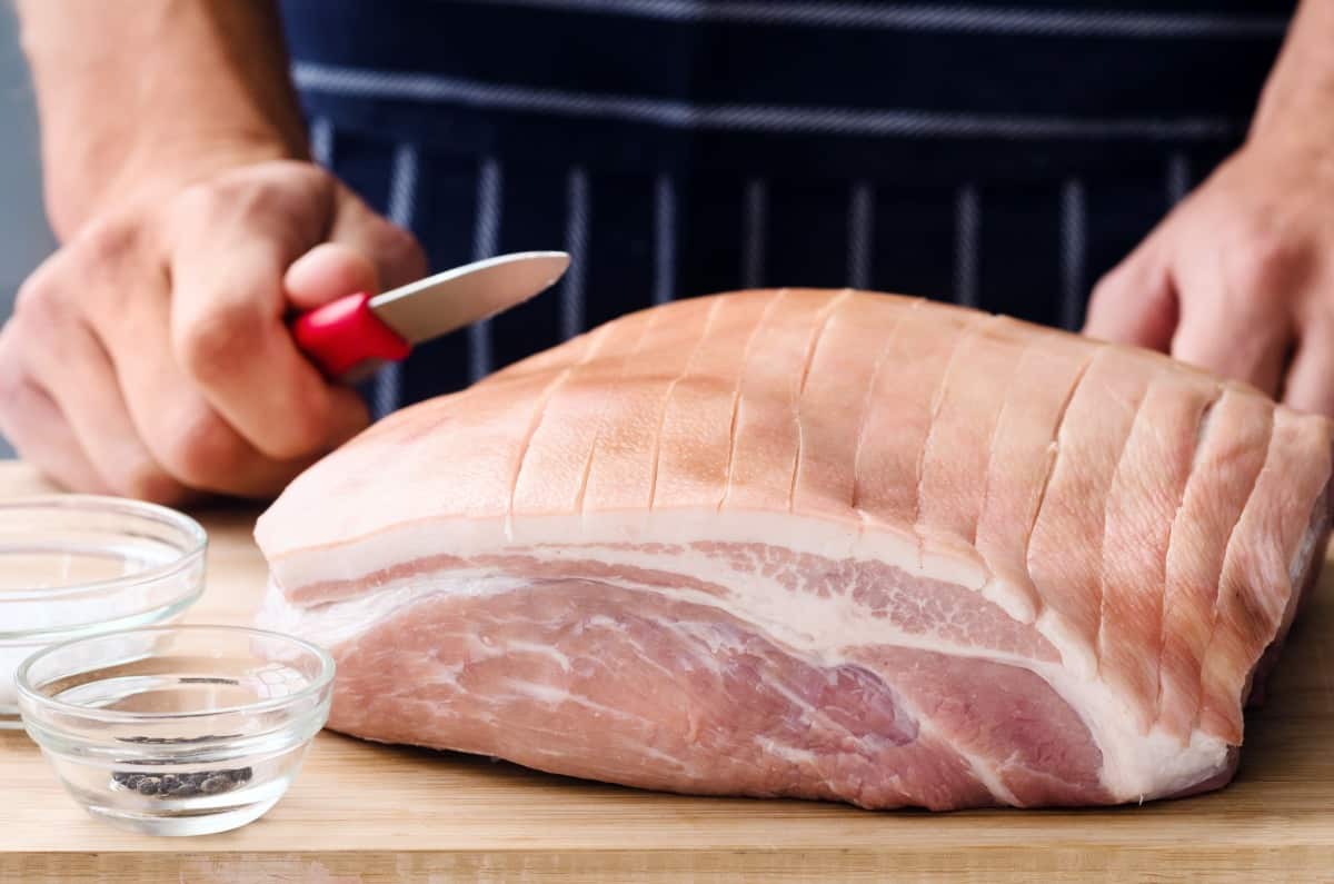 A man scoring pork skin with a small sharp kn.