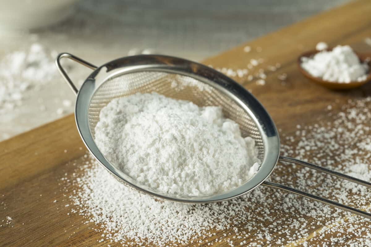 Confectioners sugar being sieved onto a wooden table