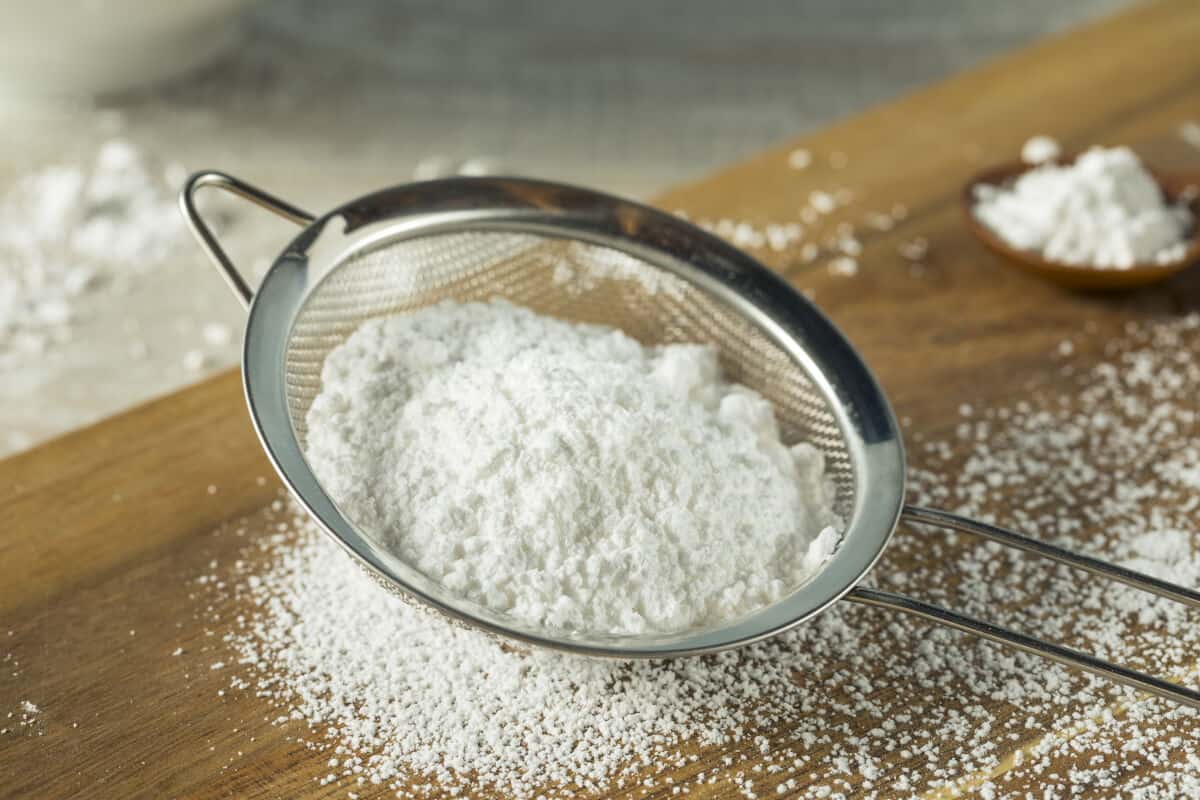 Confectioners sugar being sieved onto a wooden ta.