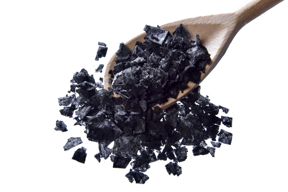 A spoon full of Cyprus black flake salt isolated on wh.