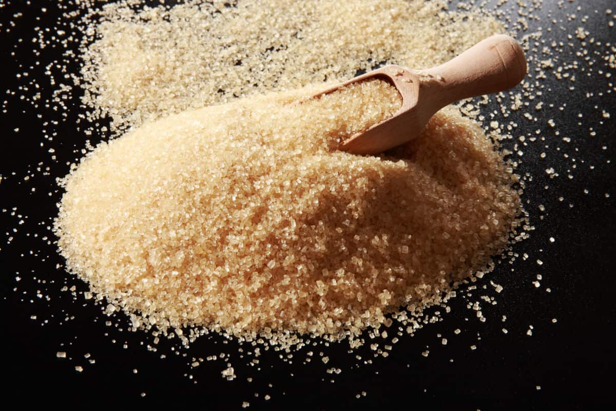 A pile of demerara sugar on a table, with a wooden scoop dug into the s.