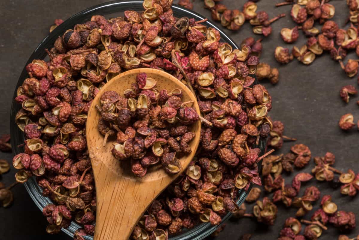 A pile of Szechuan peppercorns, with some held in a wooden sp.