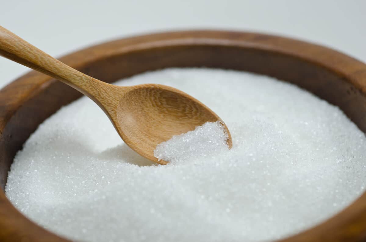 A bowl of granulated white sugar with a wooden spoon in it.