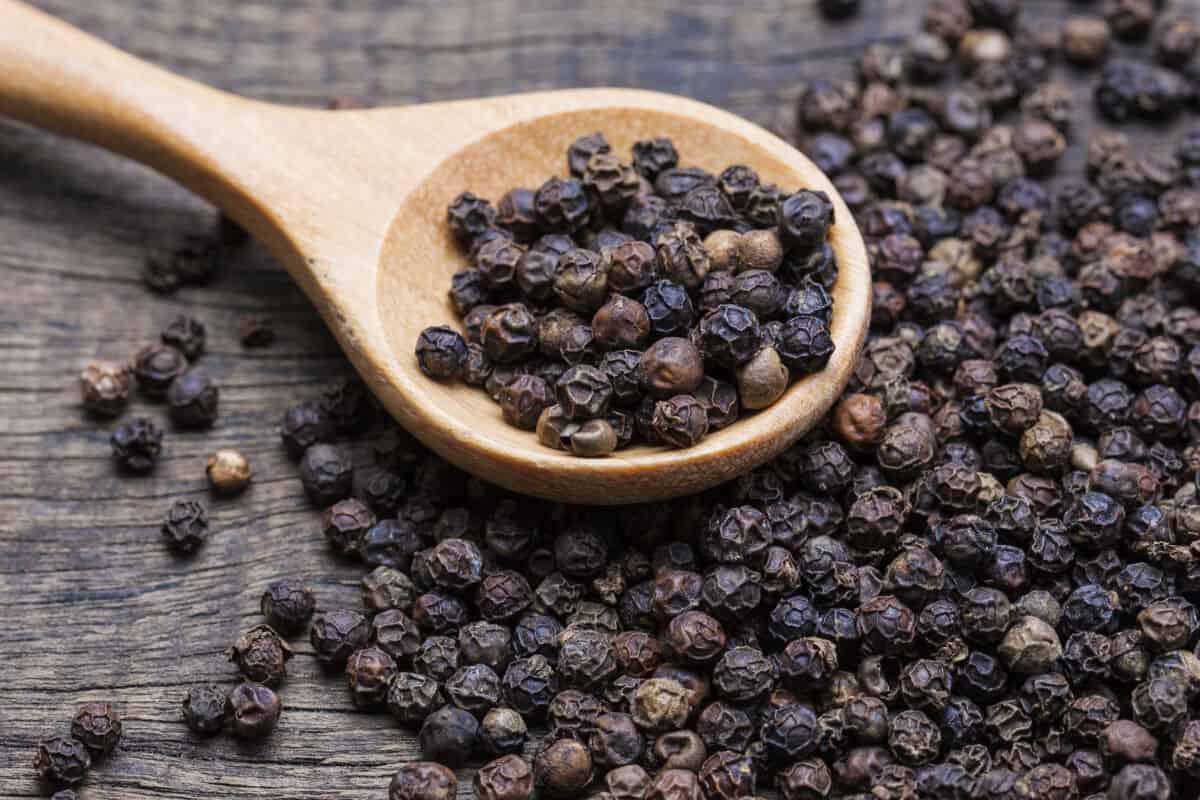 Black peppercorns in a wooden spoon, and spread over a wooden ta.