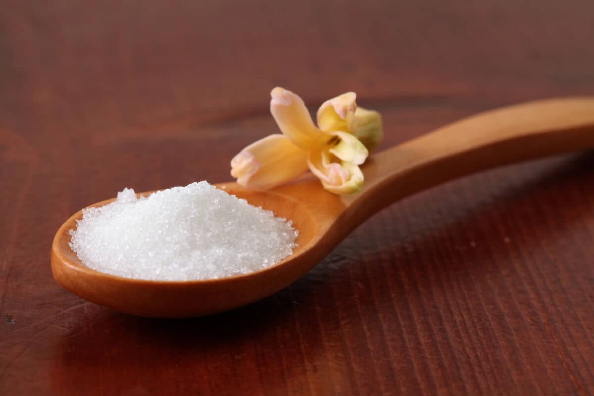 A wooden spoon with a flower on the handle full of caster su.