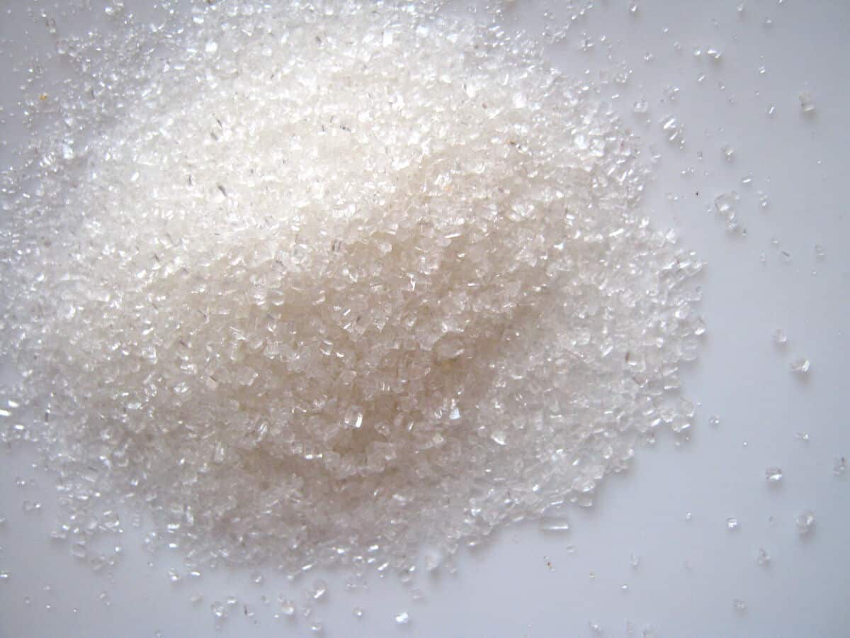 A pile of coarse sugar granules on a white surf.