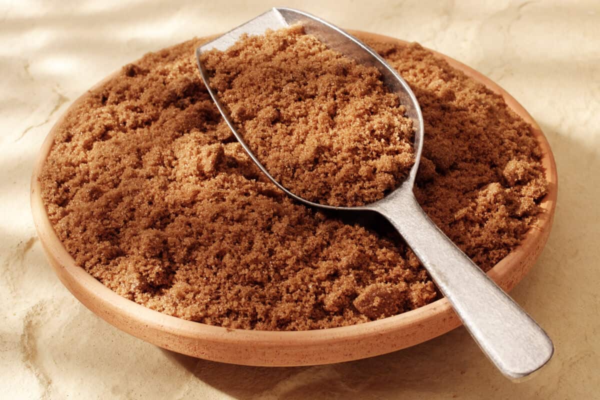 A metal scoop full of dark brown sugar in a wooden b.