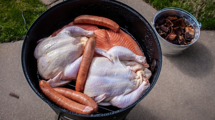 A drum style barrel smoker with chicken and sausage on the top grate.