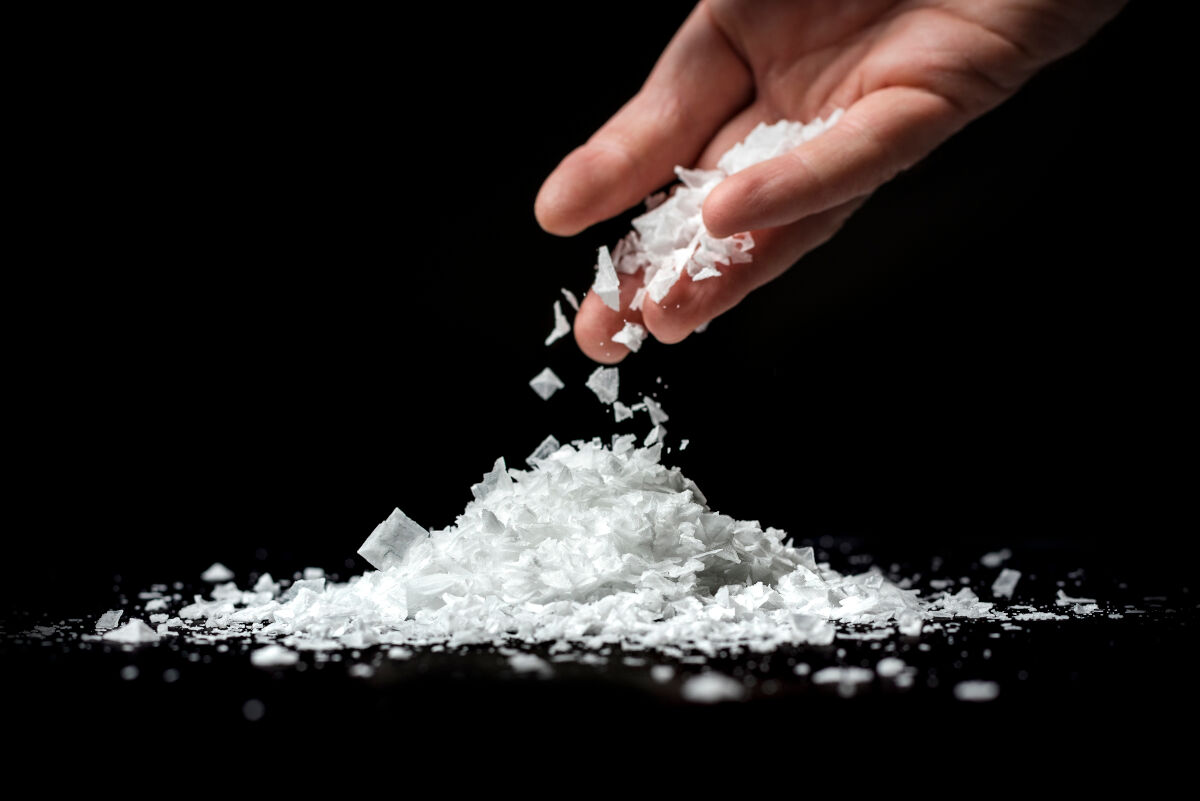 Flake salt being sprinkled into a heap on a table by a mans h.