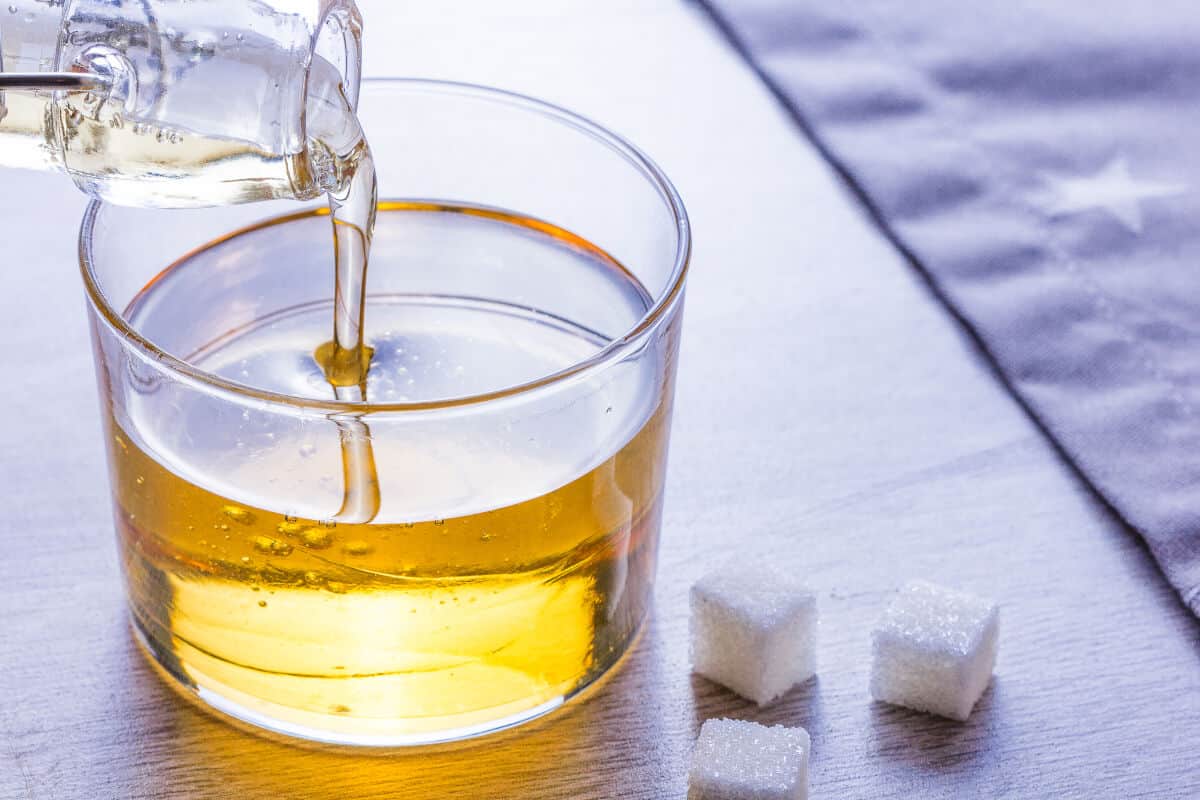 Inverted sugar being poured into a glass that is sitting next to sugar cu.