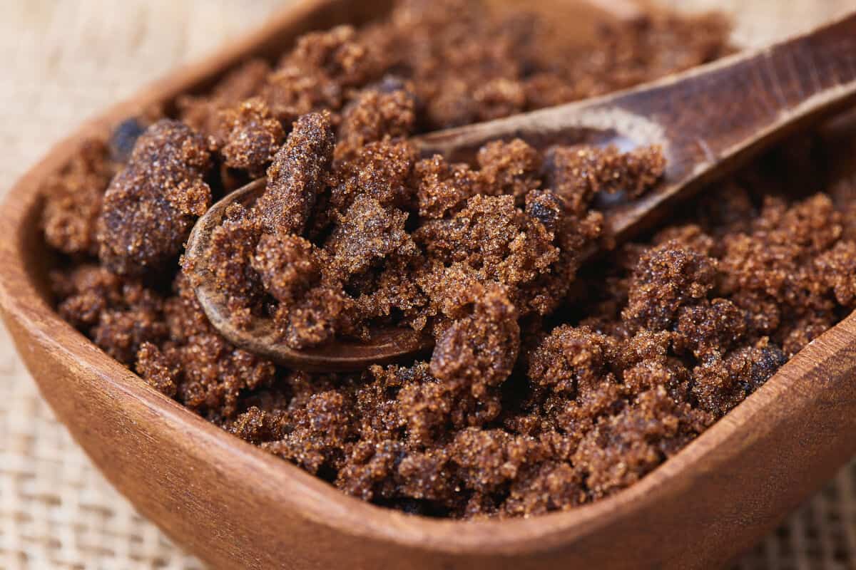 A square wooden bowl full of dark muscovado su.