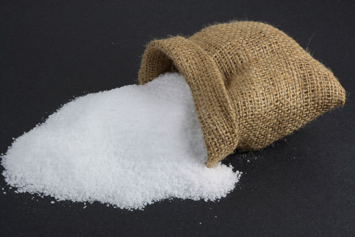 A small sack full of pickling salt fallen onto its side and spilling .