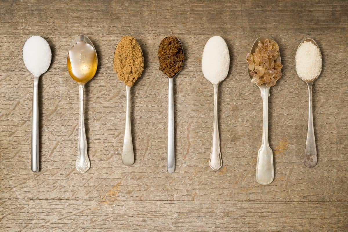 7 lined up teaspoons full of different types of su.