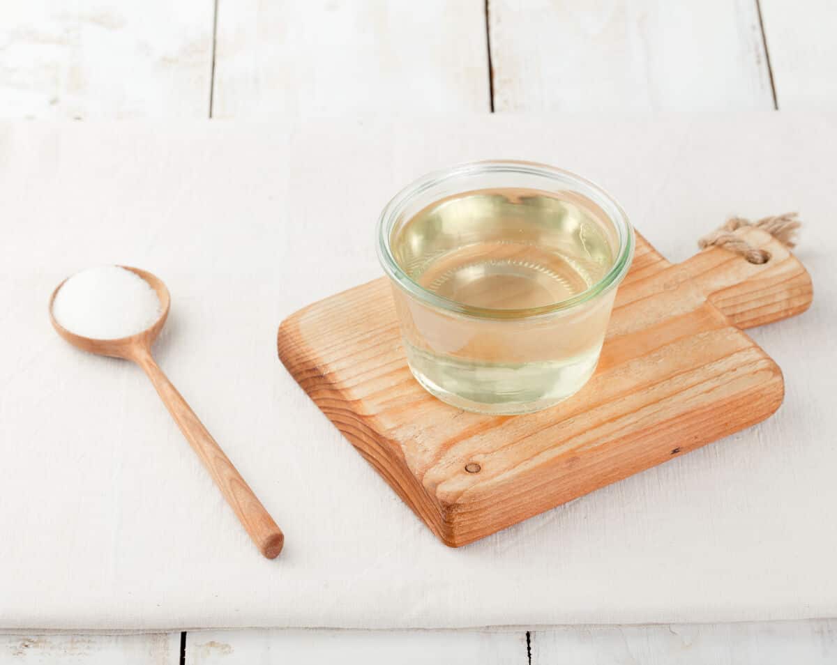 A small glass of simple sugar syrup sat on a wooden paddle, next to a spoonful of su.