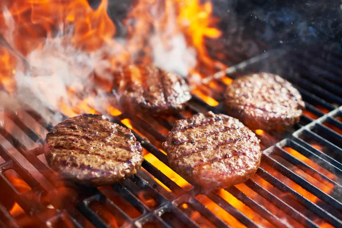 A few burgers grilling over big fla.